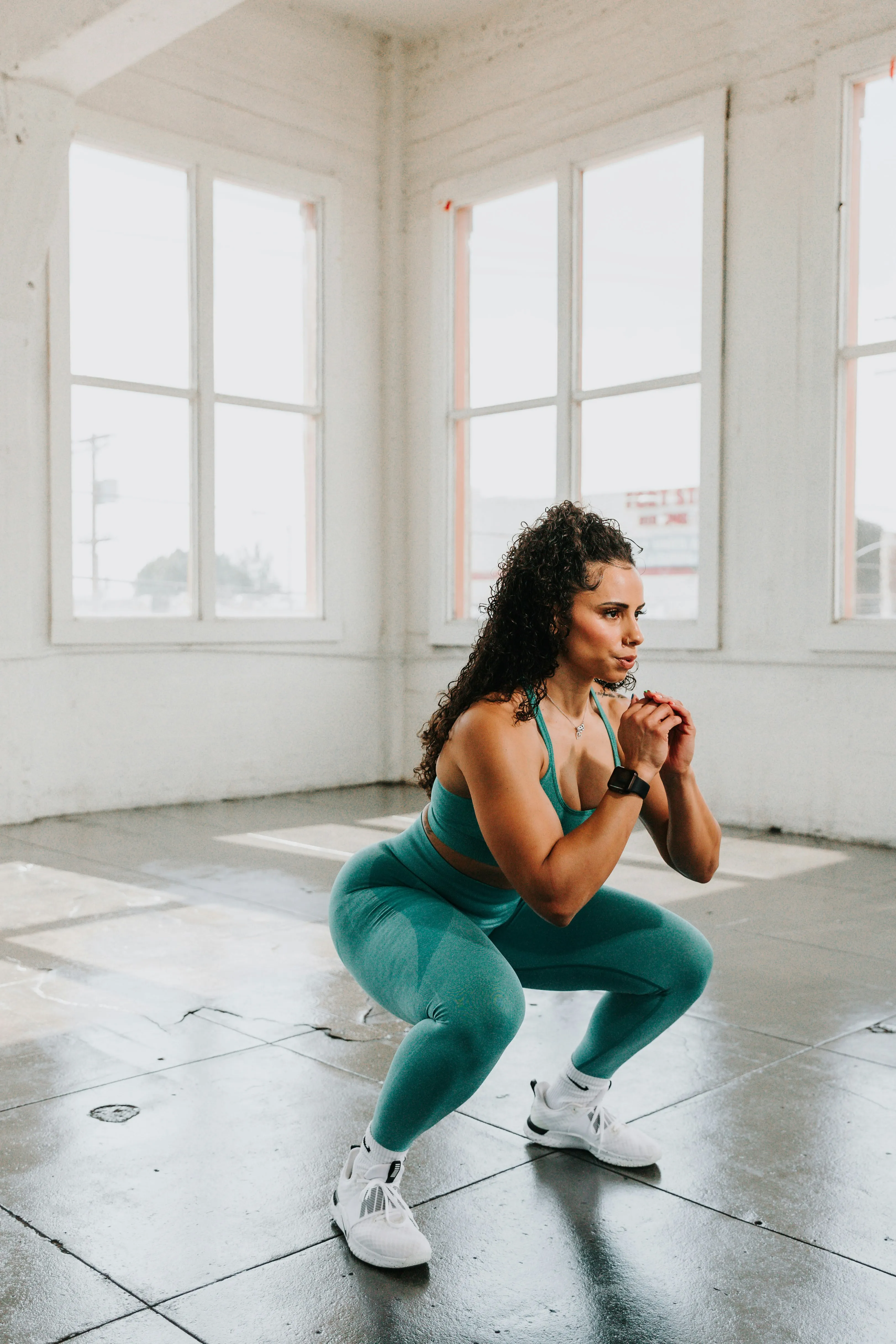 Woman squatting in workout studio wearing green activewear